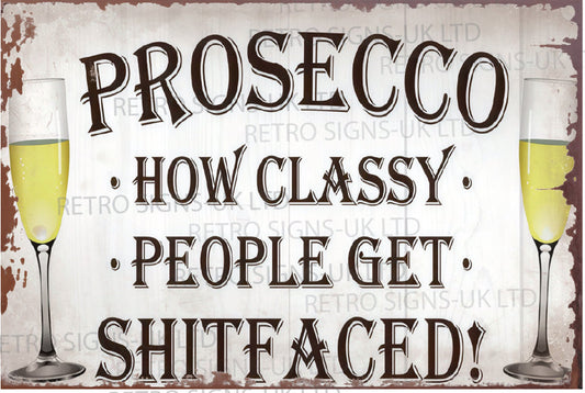 A rectangular vintage-style metal sign with the phrase “PROSECCO • HOW CLASSY • PEOPLE GET • SHITFACED!” in large dark lettering on a distressed off-white background. Two champagne glasses filled with pale yellow drink appear at the left and right edges.